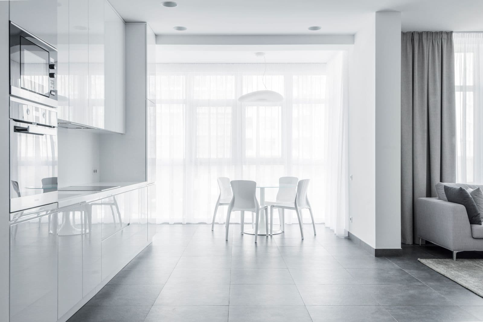 A light dining area with a small table and chairs beside tall windows and a clean tiled floor.