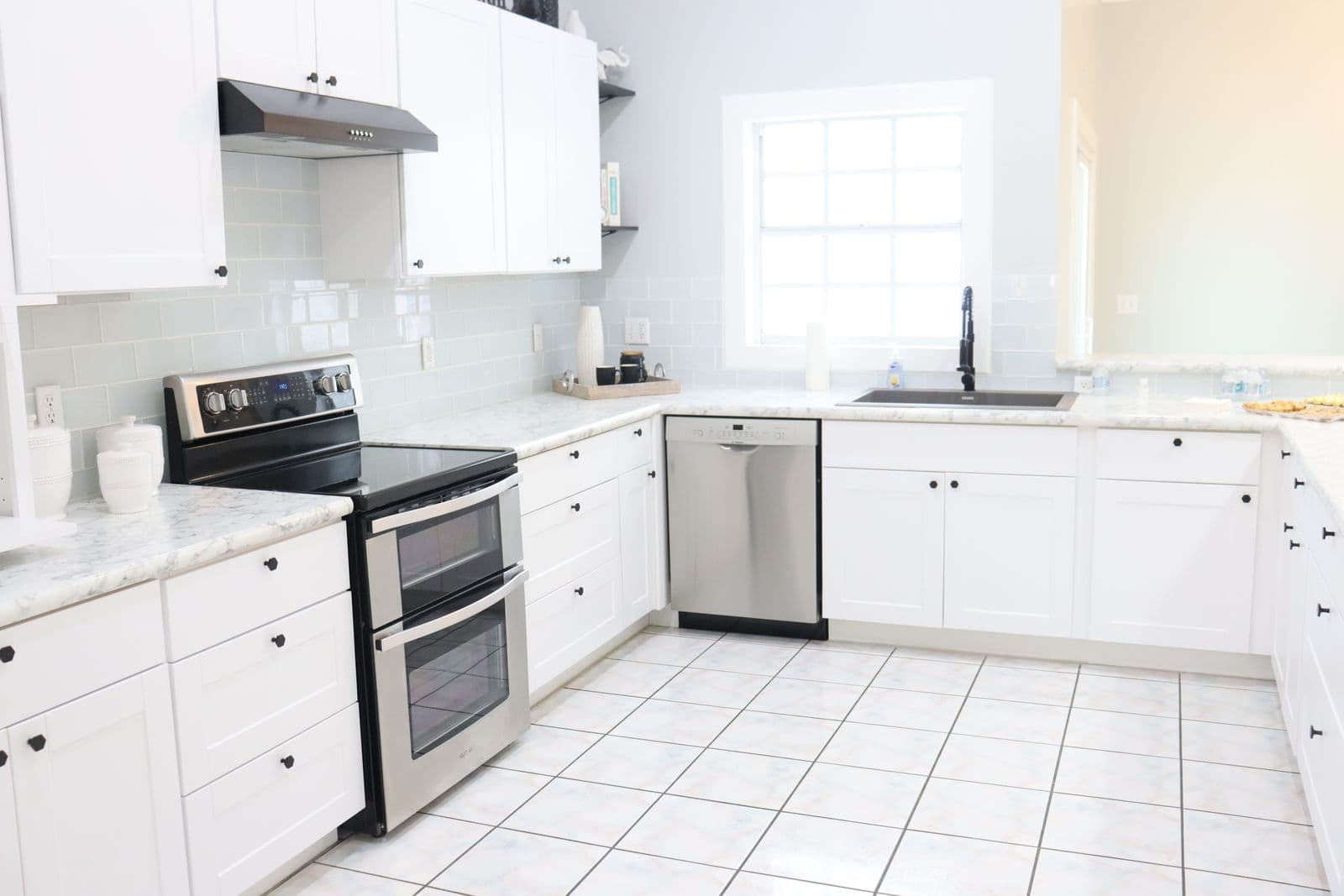 A spotless white kitchen with clear countertops, stainless steel appliances and a tiled floor.