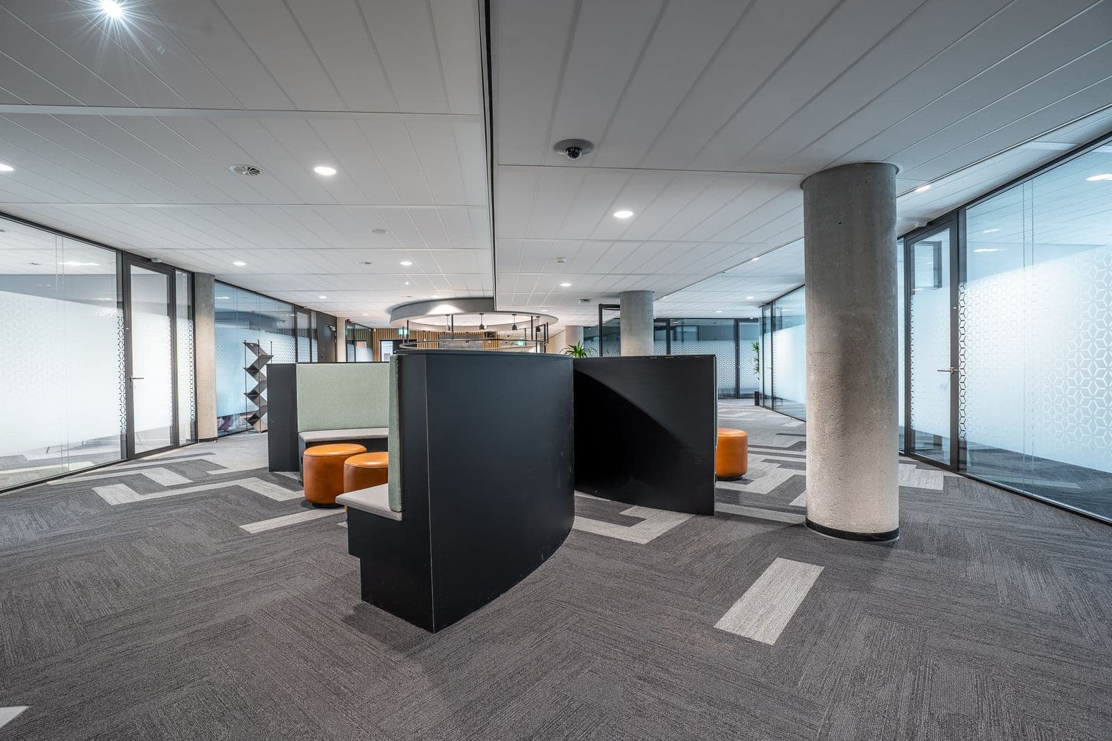 An open-plan office floor with workstations, carpet tiles and clean glass partitions.